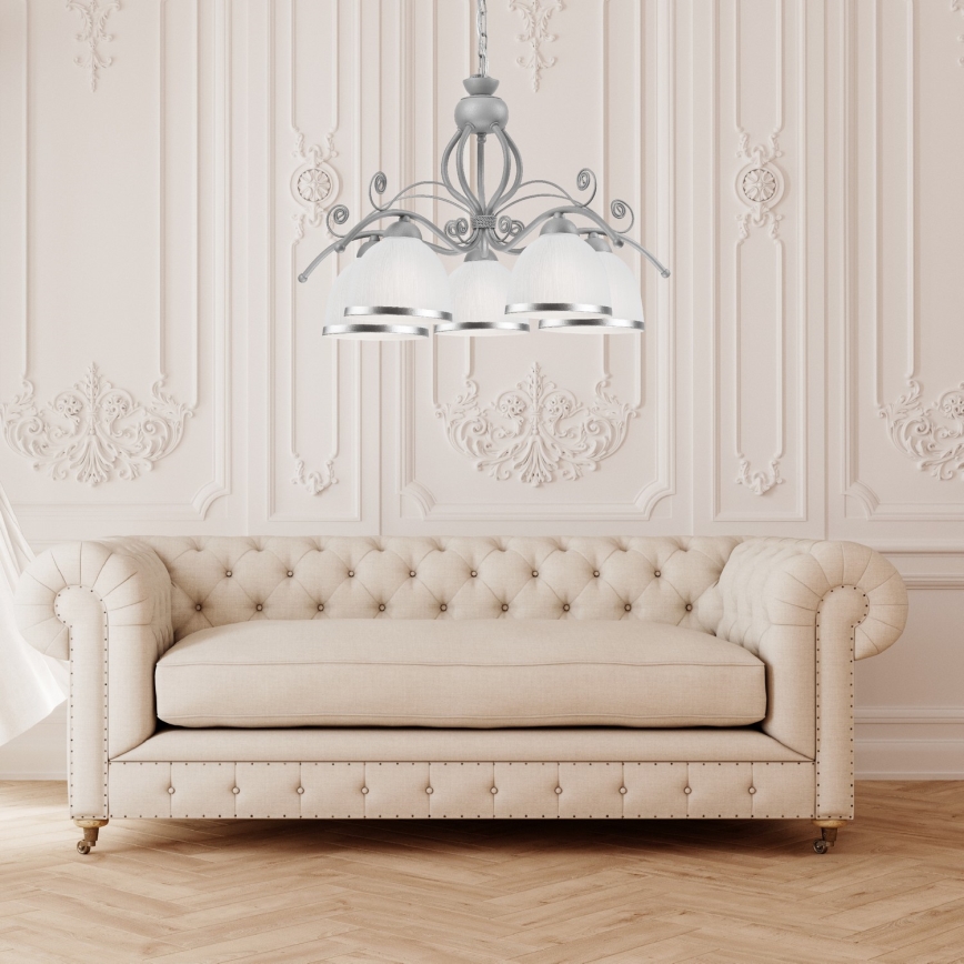 Stropná lampa s viacerými tienidlami visí nad pohovkou. Lampa je strieborno-šedá s bielymi tienidlami. Pohovka je svetlo béžová, čalúnená, v klasickom štýle. Nachádza sa v miestnosti s bielymi stenami a ozdobnými lištami.