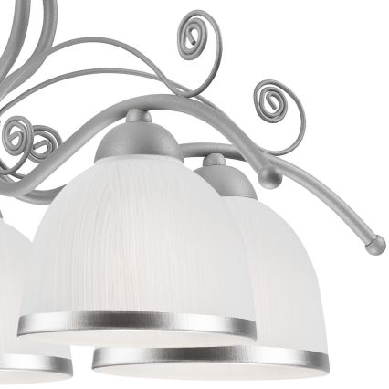 Stropné svietidlo s krivolakým kovovými ramenami a niekoľkými bielymi sklenenými tienidlami s ozdobným strieborným lemom visí v bielom priestore.