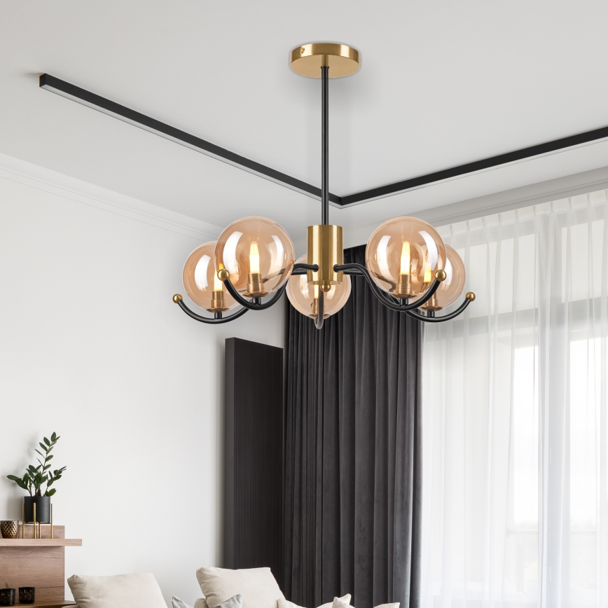 Lampa svieti v interiéri. Má päť guľových tienidiel z dymového skla a čierne kovové ramená s mosadznou úpravou. Je zavesená na strope v miestnosti s tmavými závesmi.