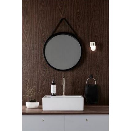 Okrúhle zrkadlo visí na stene. Pod ním je umiestnená obdĺžniková umývadlová misa s kohútikom a mydlom. Vedľa je uterák a malá svietidlo. V pozadí je hnedá drevená stena.