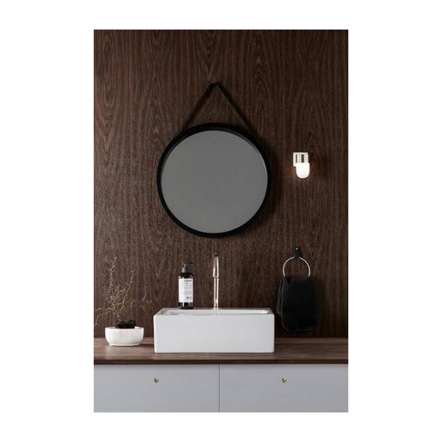 Okrúhle zrkadlo visí na stene. Pod ním je umiestnená obdĺžniková umývadlová misa s kohútikom a mydlom. Vedľa je uterák a malá svietidlo. V pozadí je hnedá drevená stena.