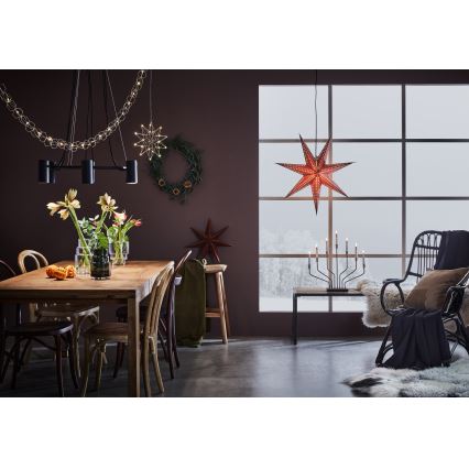 Drevený jedálenský stôl s kreslami je osvetlený modernou závesnou lampou. V miestnosti sú vianočné dekorácie: hviezdy, veniec. Pozadí tvorí okno s výhľadom na zasneženú krajinu a krémový kožušinový koberec.