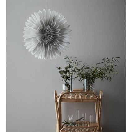 Veľká sivá papierová ozdoba visí zo stropu. Na dvojplošnom ratanovom vozíku sú vázy s kvetmi a sviečka.