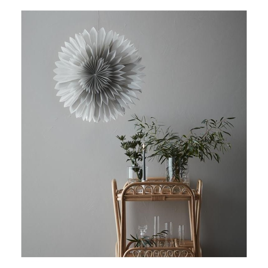 Veľká sivá papierová ozdoba visí zo stropu. Na dvojplošnom ratanovom vozíku sú vázy s kvetmi a sviečka.