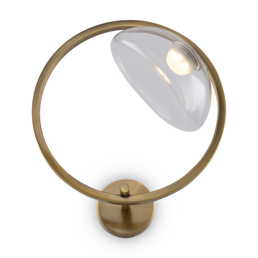 Nástenná lampa s okrúhlym kovovým rámom drží sklenený tienidlo. Lampa je pripevnená na stenu, tienidlo je čiastočne sklopené. Tienidlo je priehľadné, vnútri je viditeľná žiarovka.
