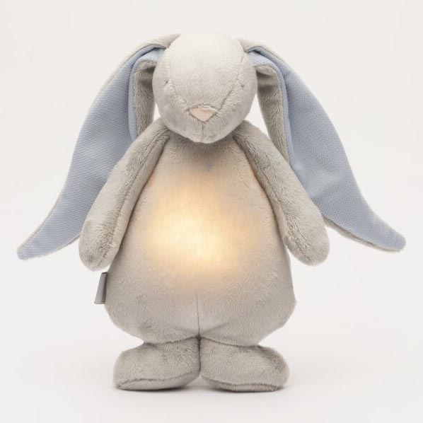 Plyšový zajačik s modrými ušami svieti jemným svetlom. Zajačik stojí na bielom pozadí.