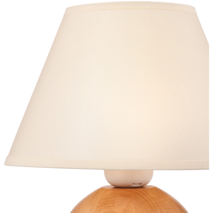 Stolová lampa s krémovým tienidlom je umiestnená na drevenom podstavci. Tienidlo je kužeľovité a prilieha na guľovitý drevený základ.