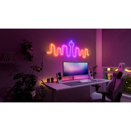 Neonové svetlo v tvare mestskej panorámy svieti na stene hernej izby. Svetlo je umiestnené nad herným stolom s počítačom, reproduktormi, klávesnicou a hereckou stoličkou. Izba je slabo osvetlená, prítomné sú rastliny.