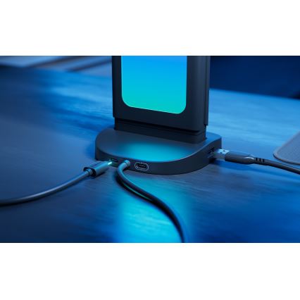 Do nabíjacej stanice sú zapojené káble USB-C a USB-A. Stanica s podsvieteným displejom je umiestnená na tmavom stole.