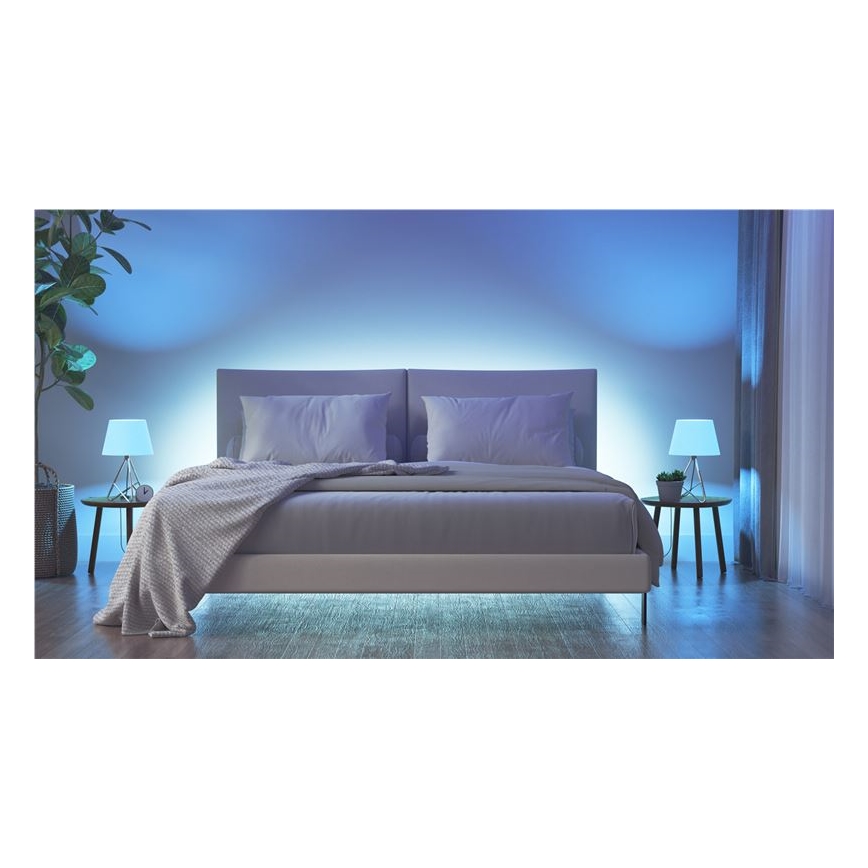 Dvojposteľ stojí v spálni. Je presvietená modrým svetlom z LED pásu umiestneného pod posteľou a za ňou. Po oboch stranách postele sú nočné stolíky s malými stolnými lampami.