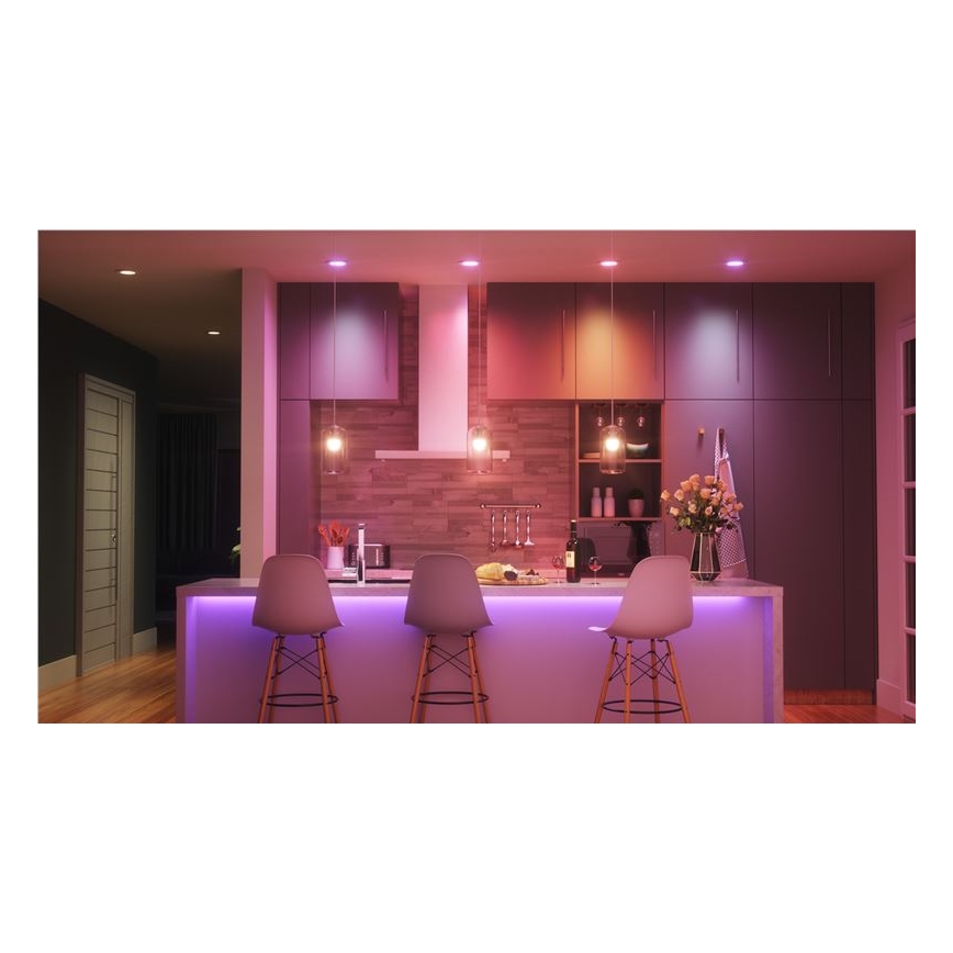 Kuchynská linka s tromi stoličkami je osvetlená farebnými LED svetlami, stropnými svietidlami a LED pásom pod linkou. Svetlá majú rôzne odtiene ružovej a oranžovej. V pozadí sú kuchynské skrinky a drevená stena.