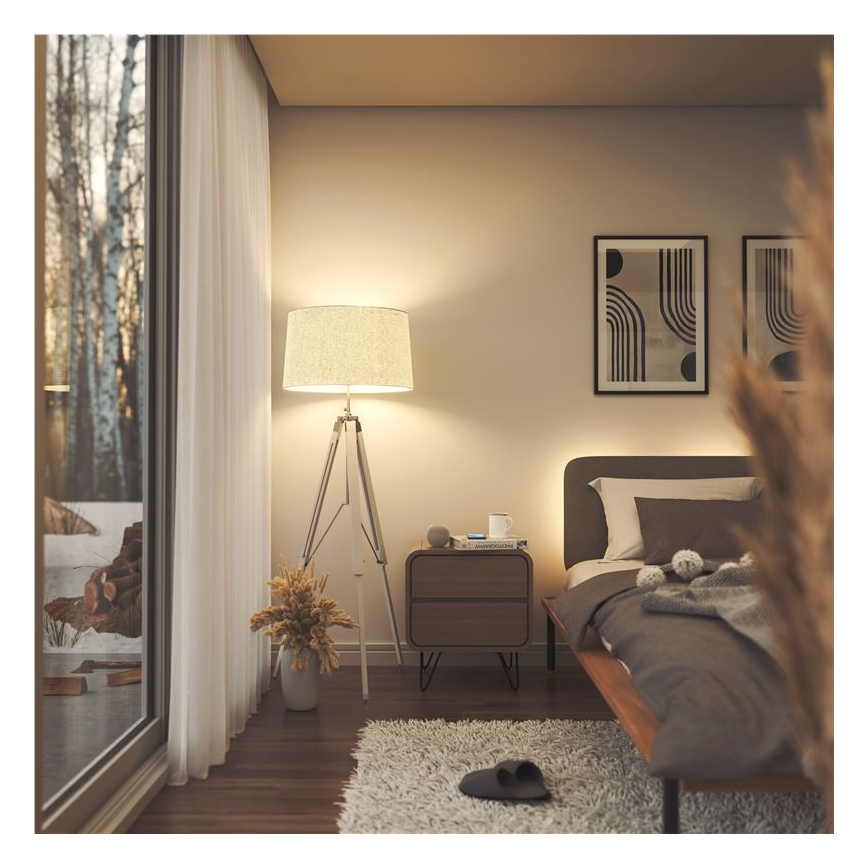 Stojacia lampa s textilným tienidlom svieti v spálni. Vedľa nej je nočný stolík s knihou a hrnčekom. V pozadí je posteľ s posteľnou bielizňou a oknom s výhľadom na vonkajšiu scénu.