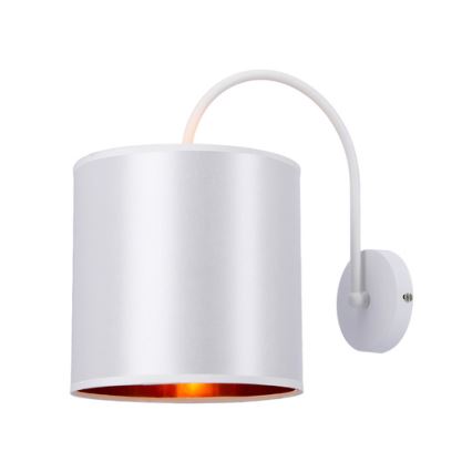 Biela nástenná lampa s valcovým tienidlom a vnútorným medeným lemom svieti. Lampa je pripevnená k stene ohnutou bielou konzolou.