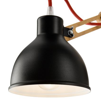 Čierna kovová lampa s tienidlom v tvare kužeľa visí na drevenom rameni s červenou textilnou šnúrou. Lampa je pripevnená k rameni pomocou kovového držiaka.