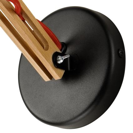 Drevená nástenná lampa s červeným textilným káblom je pripevnená k čiernemu kruhovému držiaku. Lampa je upevnená skrutkou.