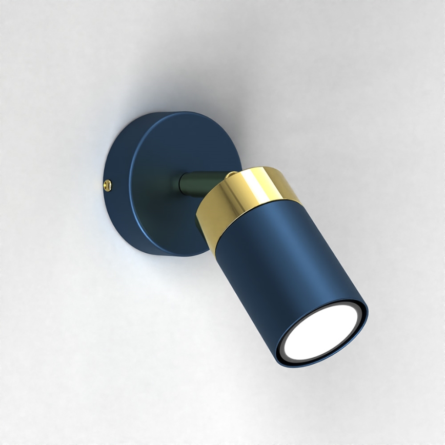 Nástenná lampa svieti. Je tmavomodrej farby s pozláteným detailom. Upevnená je na svetlej stene.