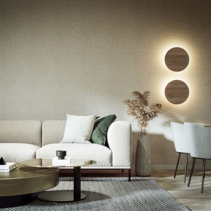 Biela sedačka stojí v obývacej izbe s hnedou textíliou na stene a dvoma kruhovými svietidlami. Pred sedačkou je nízky konferenčný stolík a koberec. V blízkosti je jedálenský kút s dvoma stoličkami.