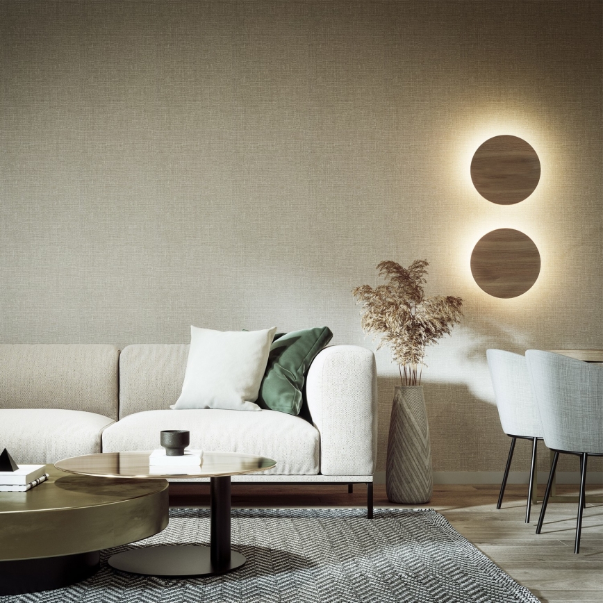 Biela sedačka stojí v obývacej izbe s hnedou textíliou na stene a dvoma kruhovými svietidlami. Pred sedačkou je nízky konferenčný stolík a koberec. V blízkosti je jedálenský kút s dvoma stoličkami.