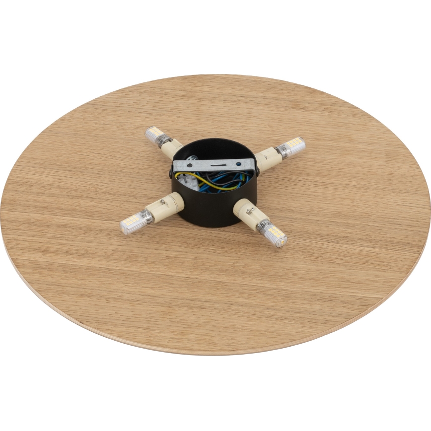 Svietidlo s kruhovou drevenou doskou, v strede má čierny kovový kryt s pripojenými štyrmi LED žiarovkami. Elektrické káble sú viditeľné vnútri krytu.