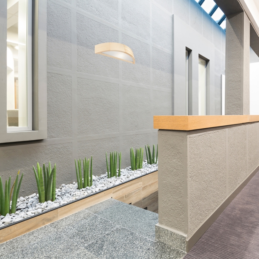 Drevený rám obklopuje svetelný zdroj. Rám je svetlohnedý, zakrivený a má viditeľnú štruktúru dreva. Svetelný zdroj je čiastočne viditeľný cez priesvitnú časť.