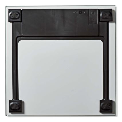 Váha z bezpečnostného skla leží na bielom pozadí. Na zadnej strane je viditeľný čierny mechanizmus s vypínačom. Na okrajoch sú umiestnené protišmykové nožičky.