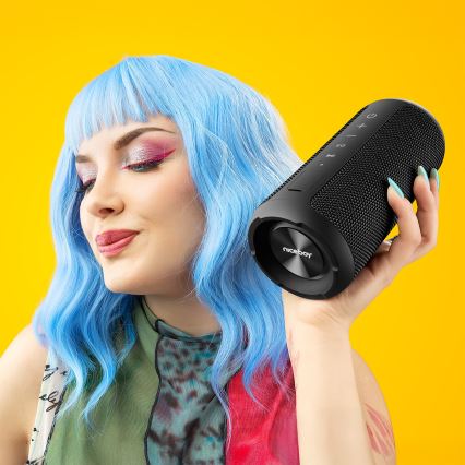 Žena s modrými vlasmi drží v ruke čierny prenosný reproduktor Niceboy. Reproduktor je valcovitého tvaru s viditeľnými ovládacími tlačidlami. Pozadie je žlté.