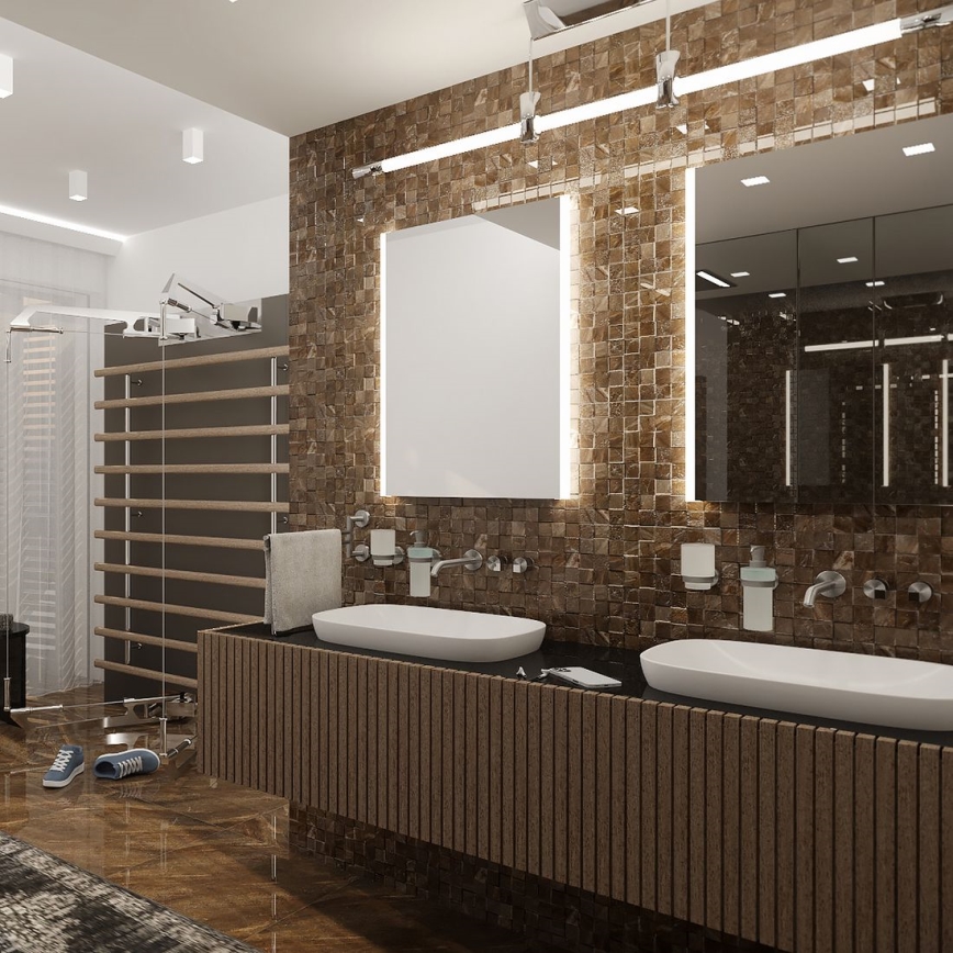 Dve umývadlá sú umiestnené na drevenom nábytku v kúpeľni. Steny sú obložené hnedými dlaždicami, nad umývadlami sú zrkadlá s podsvietením. V pozadí je viditeľná časť posilňovne s dreveným náradím na cvičenie.