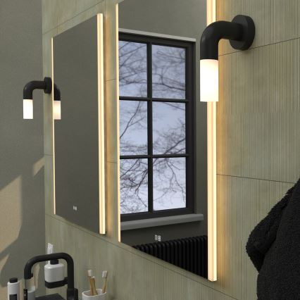 Zrkadlo s integrovaným LED osvetlením je umiestnené v kúpeľni. Po stranách zrkadla sú umiestnené ďalšie nástenné LED svietidlá. V pozadí je vidieť okno s holými stromami.