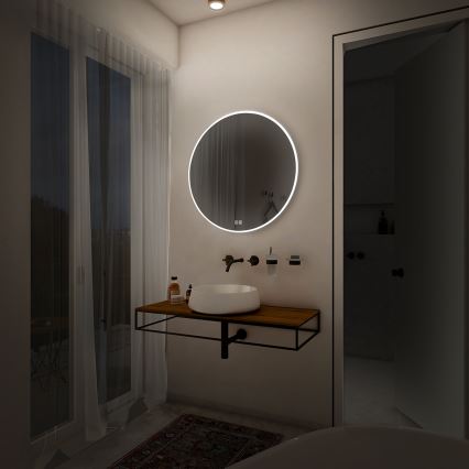 Okrúhle zrkadlo so zabudovaným osvetlením je umiestnené v kúpeľni nad drevenou umývadlovou skrinkou. Vedľa zrkadla je umývadlo a batéria. Kúpeľňa má svetlé steny a dvere vedúce do ďalšej miestnosti.