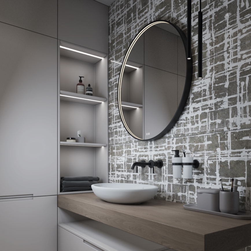 Kúpeľňová umývadlová misa s batériou je umiestnená na drevenom pulte pred veľkým okrúhlym zrkadlom so vstavaným podsvietením. Steny sú obložené dlaždicami s abstraktným vzorom. Na pulte sú aj doplnky, ako dávkovače mydla a stojan na zubné kefky.