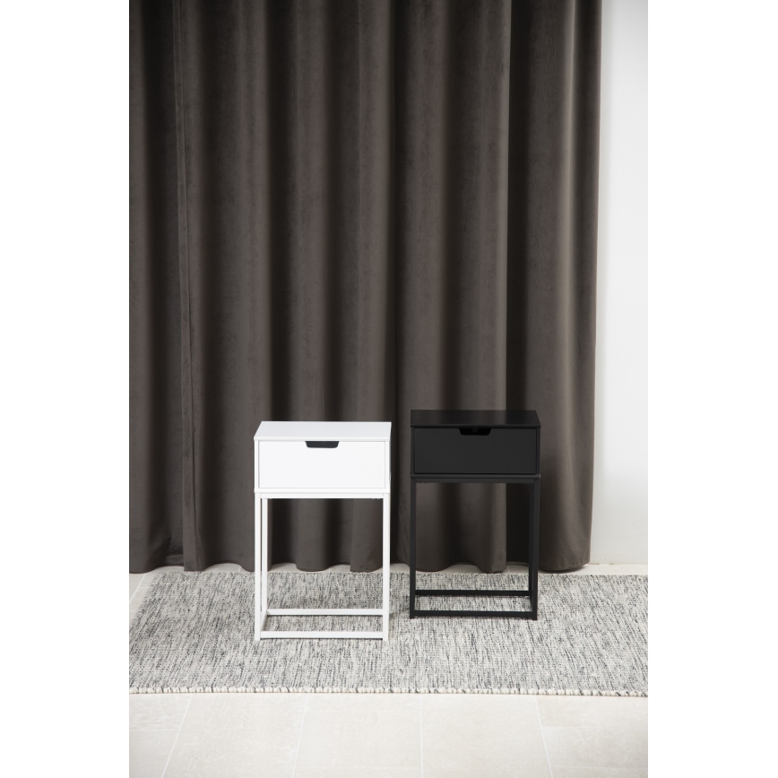 Dve nočné stolíky, jeden biely, jeden čierny, stoja na koberci pred tmavosivou záclonou. Každý má jeden šuflík.