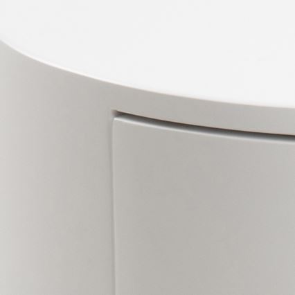 Biela nočná stolíka s okrúhlou doskou má jeden výsuvný šuplík. Stolíka je čiastočne viditeľná, zobrazená je jej horná časť a bočná strana so šuplíkom.