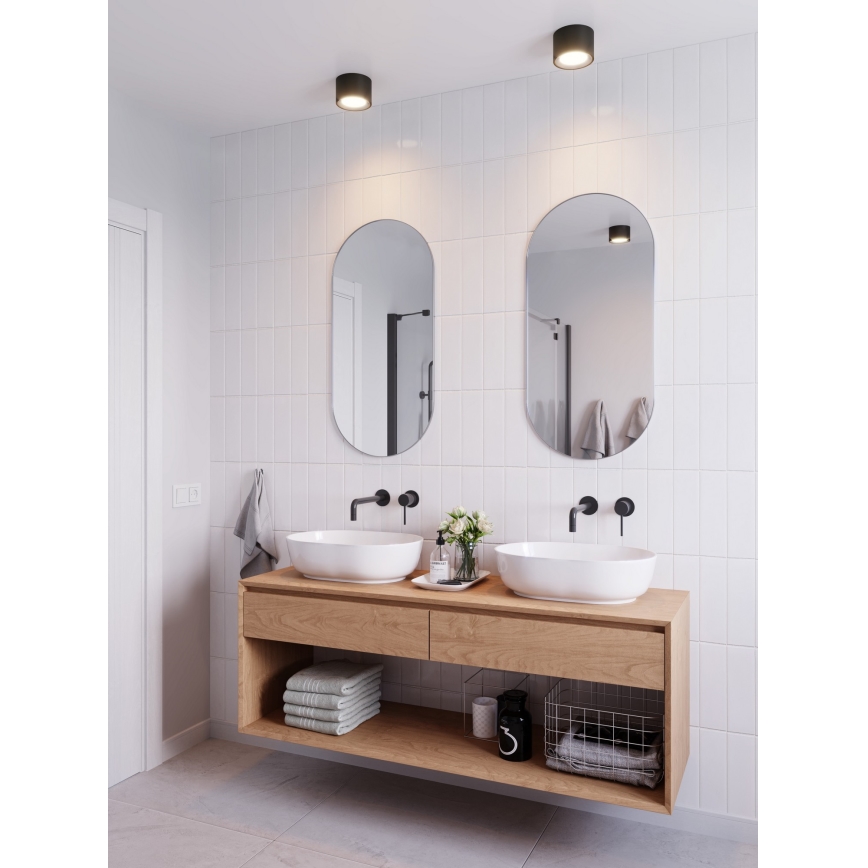 Dve umývadlá sú umiestnené na drevenom nábytku v kúpeľni. Nad nimi visia dve oválne zrkadlá. Steny sú obložené bielymi obkladačkami. Na strope sú dve bodové svetlá.