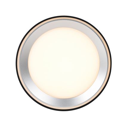 Okrúhle LED svetlo svieti. Má strieborný a béžový rámik s čiernym lemom. Svetlo je umiestnené na bielom pozadí.