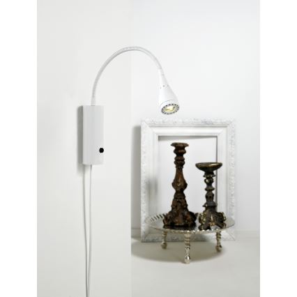 Biela nástenná lampa s ohybným ramenom smeruje svetlo na dve ozdobné svietniky na podnose. Lampa je pripevnená na stene a má vypínač na základni. Svietniky sú umiestnené v bielom ráme.