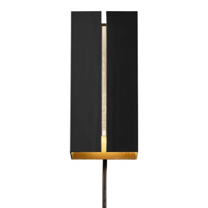 Stojacia lampa s čiernym obdĺžnikovým tienidlom s úzkou zlatou štrbinou, ktorá vyžaruje svetlo. Lampa je umiestnená na tmavom kovovom stojane pred bielym pozadím.