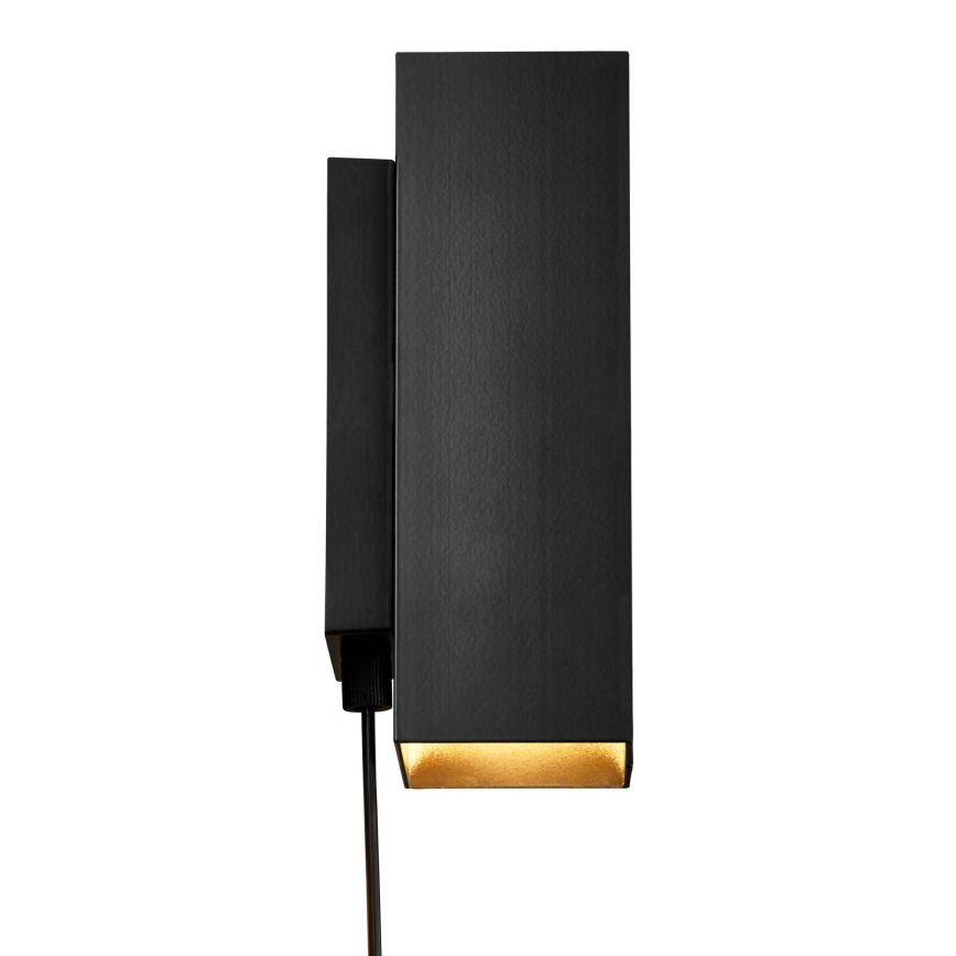 Čierna nástenná lampa svieti. Je pripojená káblom k malému čiernemu spínaču. Svietidlo má zlatú vnútornú časť.
