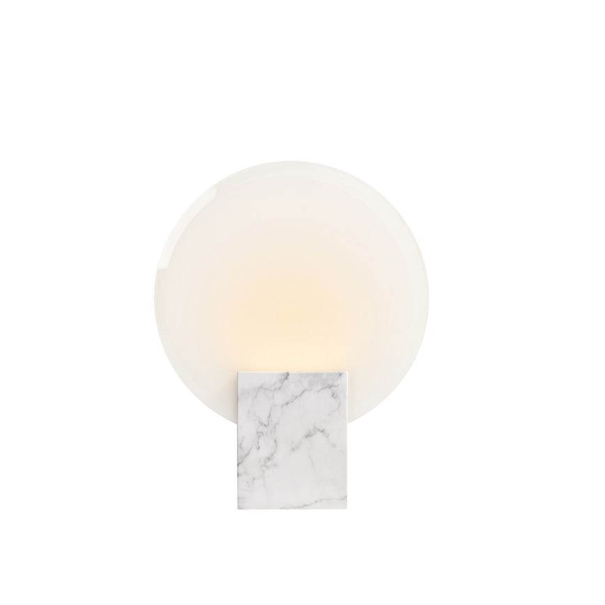 Stolová lampa svieti. Oválny, priesvitný tienidlo je umiestnené na štvorcovej mramorovej podstavci. Biele pozadie.