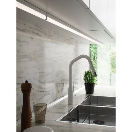 LED pásik osvetľuje kuchynskú linku s mramorovou stenou. Pásik je pripevnený pod hornými skrinkami nad drezom a pracovnou doskou. V popredí je vidieť drez, batériu a kuchynské doplnky.