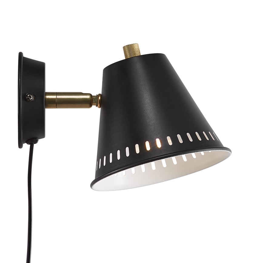 Nástenná lampa s čiernym kužeľovitým tienidlom a bielou vnútornou časťou s otvormi, pripevnená k stene pomocou mosadznej ramienka a čierneho držiaku. Lampa je pripojená na elektrický kábel.