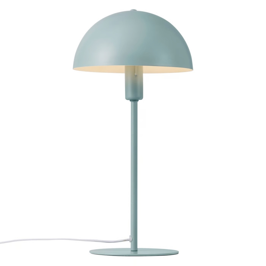 Stolová lampa s bledomodrým tienidlom v tvare huby stojí na rovnom podstavci. Lampa je pripojená na elektrickú sieť bielym káblom.