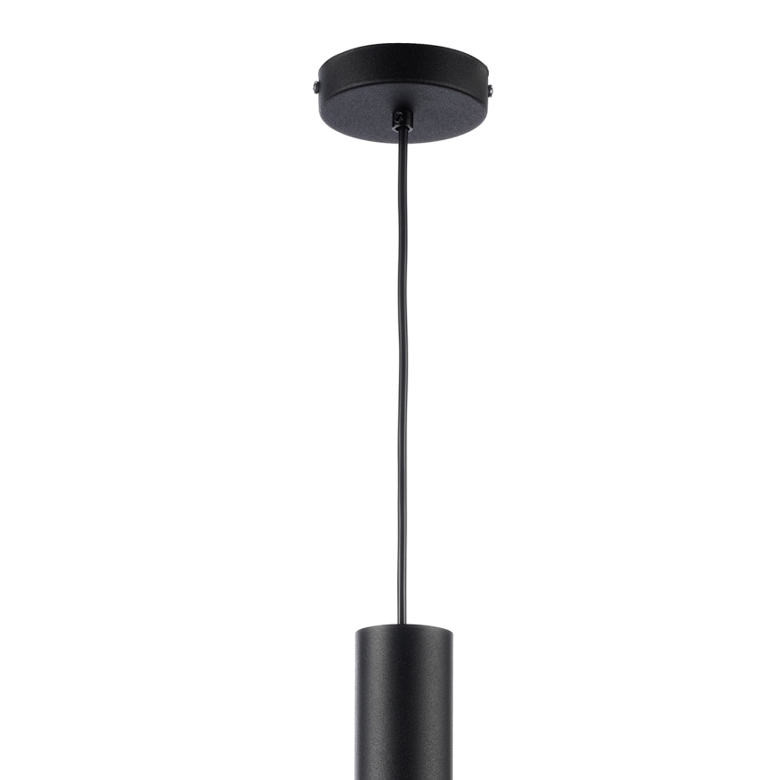 Čierna závesná lampa visí z čierneho stropného držiaka. Elektrický kábel spája držiak s valcovitým tienidlom. Pozadie je biele.