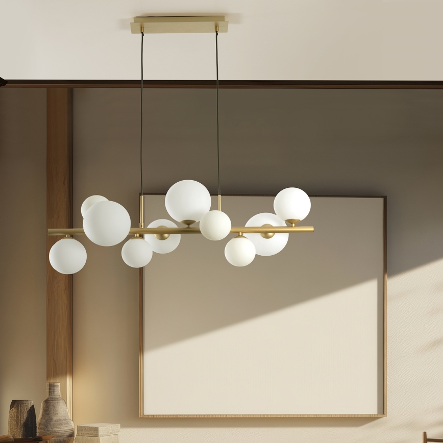 Lampa visí zo stropu. Skladá sa z zlatej tyče, z ktorej visí niekoľko mliečnobielych guľových tienidiel rôznych veľkostí. Svetlé pozadie.