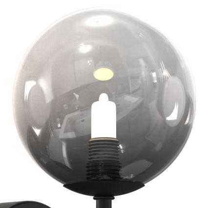 Svietidlo s guľovou tienidlom z tmavého skla chráni žiarovku. Tienidlo je pripevnené k čiernej kovovej základni. Na pozadí sa odráža kúpeľňa.