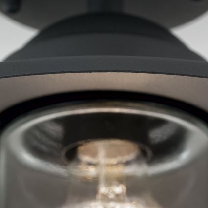 Svietidlo s tmavosivým tienidlom a skleneným difúzorom osvetľuje priestor. Žiarovka je viditeľná cez sklenený kryt. Svietidlo je pripevnené k stropu.