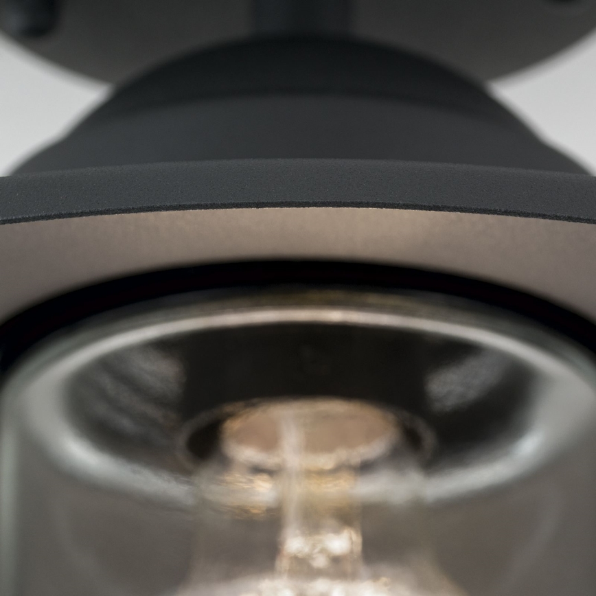 Svietidlo s tmavosivým tienidlom a skleneným difúzorom osvetľuje priestor. Žiarovka je viditeľná cez sklenený kryt. Svietidlo je pripevnené k stropu.