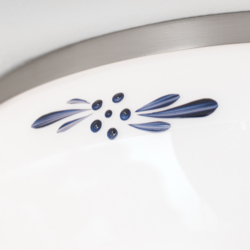 Detail biely porcelánový povrch s tmavomodrým vzorom listov a bobuliek. Vzor je umiestnený pod kovovými lemom.