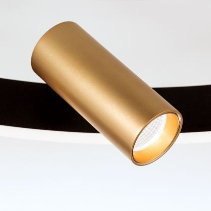 Zlatá valcová bodová lampa svieti. Je pripevnená k čiernemu a bielemu podkladu.