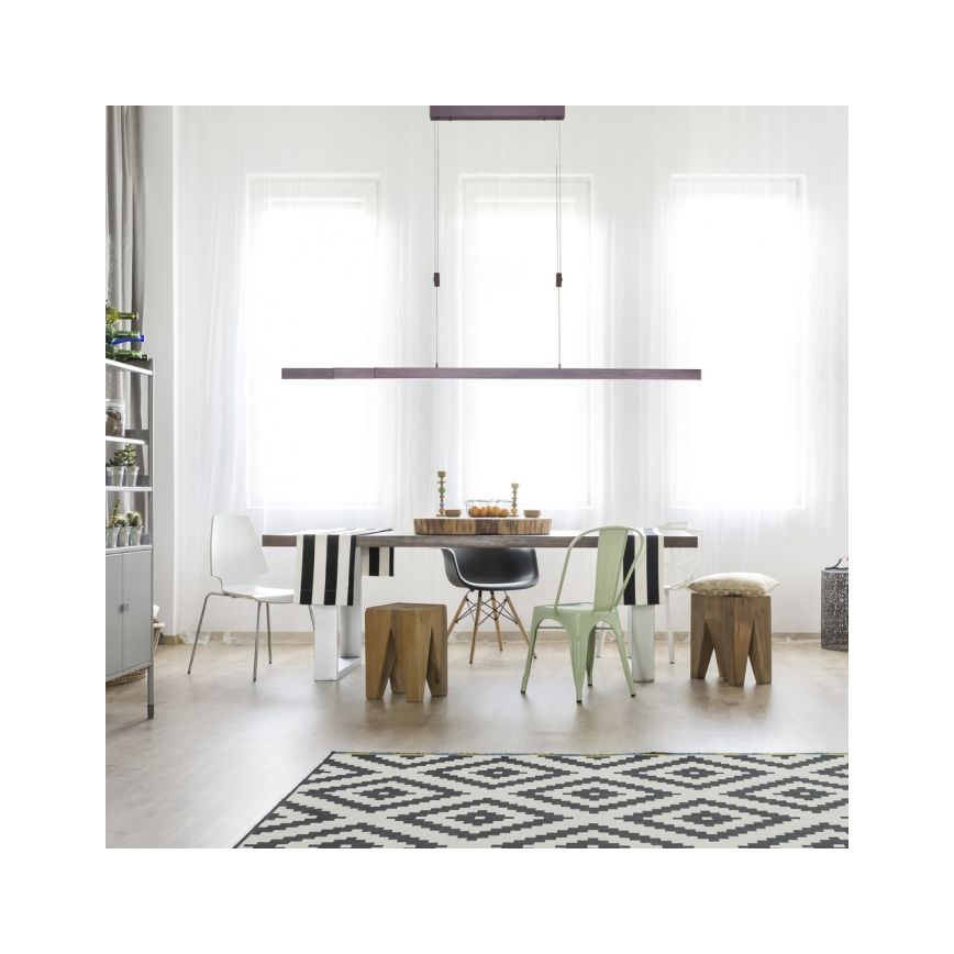 Dlhá lineárna lampa visí nad jedálenským stolom v svetlej miestnosti. Stoličky a stolík s ovocím sú umiestnené okolo stola. Podlaha je pokrytá čierno-bielym kobercom.