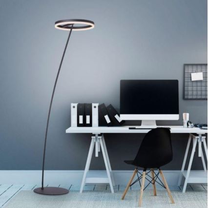 Stojacia lampa s kruhovým tienidlom stojí v pracovni. Lampa osvetľuje stôl s počítačom, kancelárskymi potrebami a stoličkou. Pozadie tvorí sivá stena.